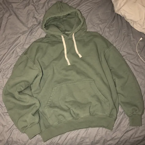 Photo du fournisseur : sweat à capuche vert froissé, posé sur un lit.